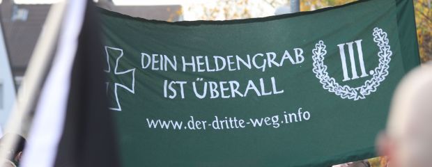 Auf dem Bild ist ein Kundgebungsbanner der Partei Der Dritte Weg mit der Aufschrift "Dein Heldengrab ist überall" zu sehen.